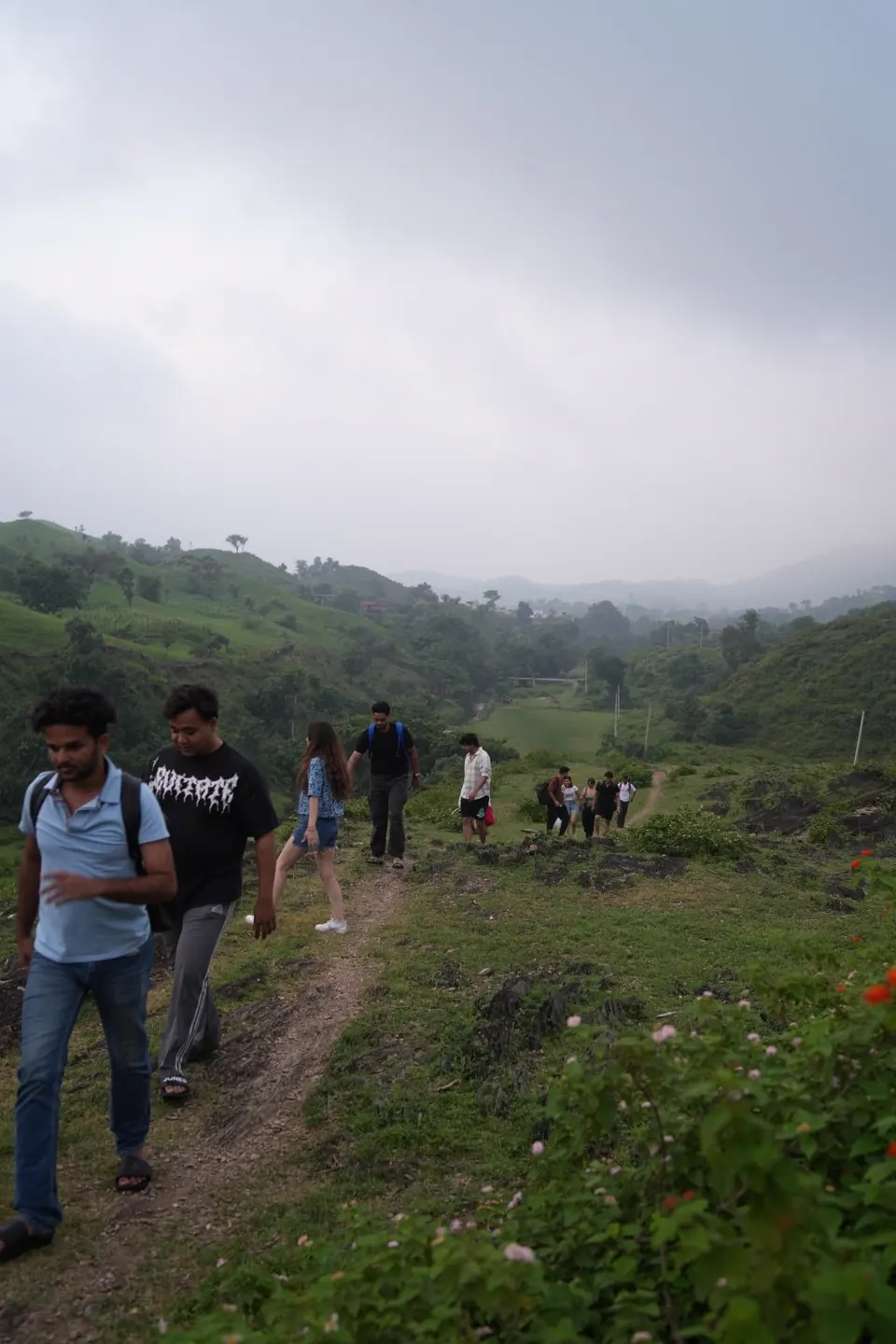 Travellers walking down a narrow trail through green monsoon hills